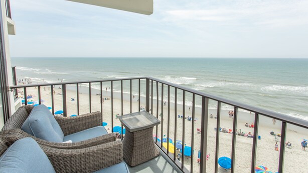 A balcony with wicker furniture overlooking a beach.