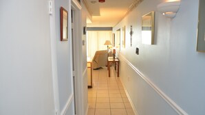 A narrow hallway with a chair and a lamp in the distance, leading to a room with a bed. - LARGE AND LOVELY! LOTS OF ROOM IN THIS 3 BEDROOM CONDO RIGHT ON THE OCEAN! (Murrells Inlet)
