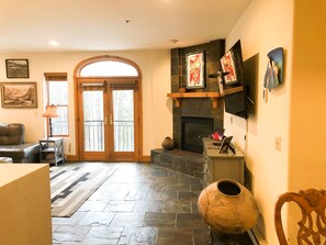A spacious living room with a fireplace, a large window, and a stone floor. - Spacious, Quiet Remodeled 3-Bedroom Mountain Chalet (Mountain Village)
