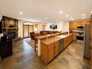 A spacious kitchen with a large island, wooden cabinets, a built-in stove, and a stone fireplace.