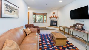 A living room with a leather sofa, a patterned rug, a wooden coffee table, a fireplace, a television, and a large framed picture on the wall.