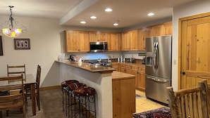 A modern kitchen with wooden cabinets, stainless steel appliances, a bar area, and a chandelier. - Pet-Friendly 1-Bedroom Condo With Pool, Hot Tubs (Mountain Village)
