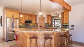 A kitchen with wooden cabinets, a stainless steel refrigerator, a large island with stools, and pendant lighting.