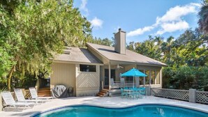 A swimming pool with a covered patio area, lounge chairs, and a table with a blue umbrella. - Short walk to the beach with great golf views! (Hilton Head)