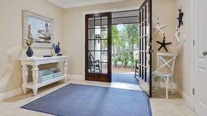 A room with a white console table, a painting, a blue mat, a door with glass panels, and starfish decorations. - Short walk to the beach with great golf views! (Hilton Head)