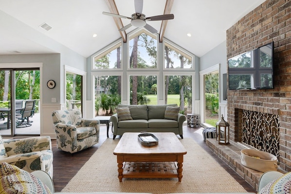 A spacious living room with a large window, a fireplace, and a ceiling fan.
