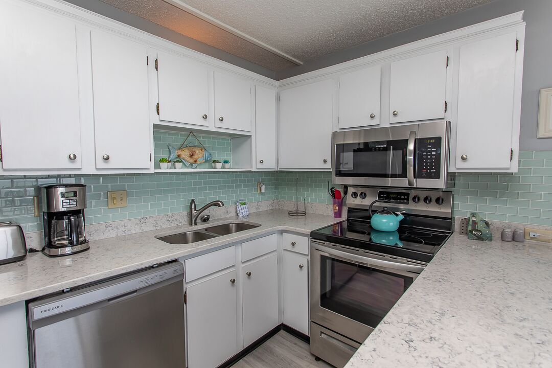 A compact kitchen with white cabinets, a stainless steel dishwasher, a double oven, and a microwave.