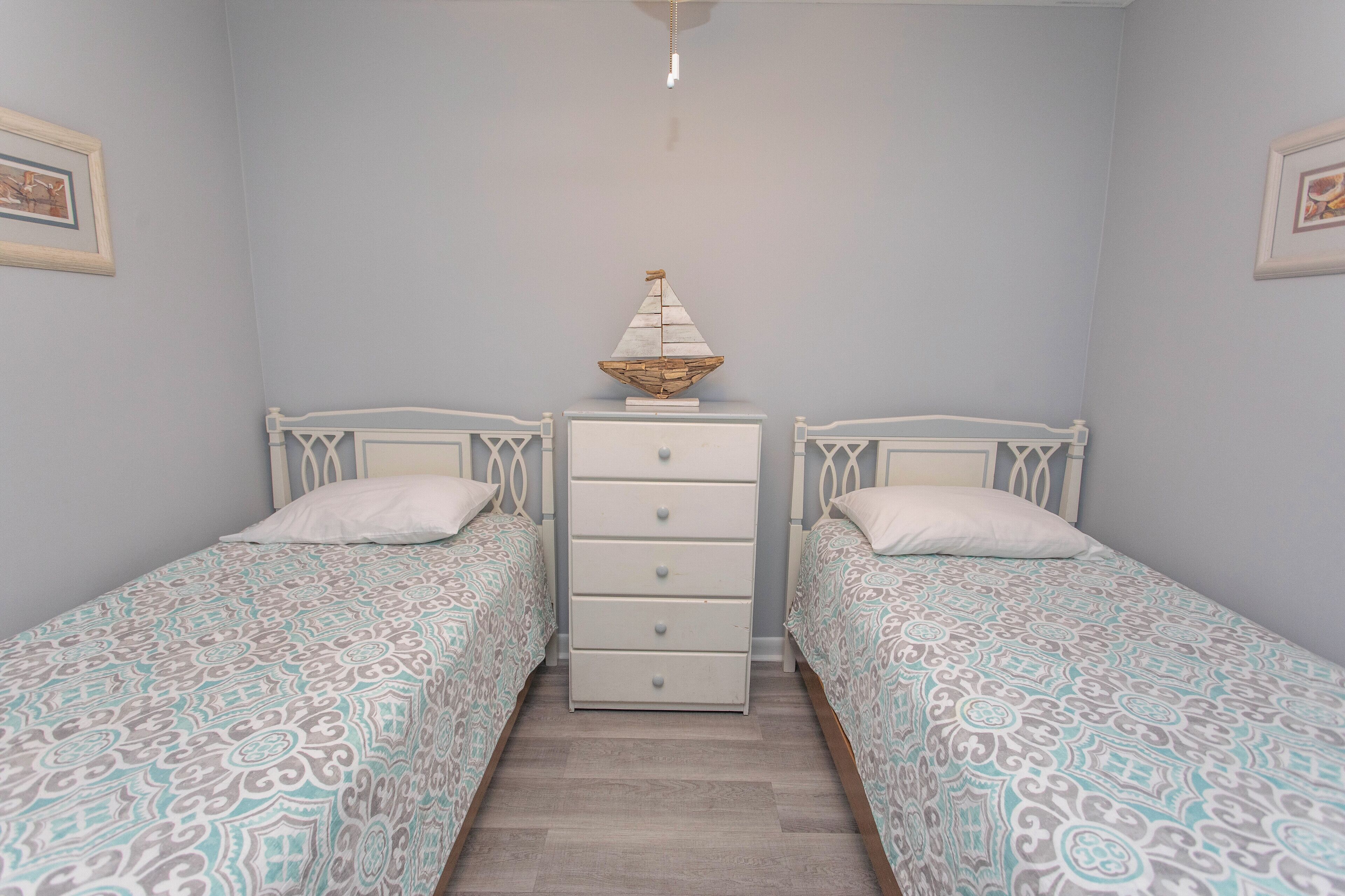 Une chambre avec deux lits simples, une commode et un objet décoratif posé sur la commode.