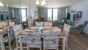 A dining area with a wooden table and chairs, a chandelier, and a large mirror reflecting the room. - OCEANFRONT LARGE 2 BEDROOM CONDO (Murrells Inlet)