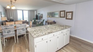 A spacious living area with a large island counter, a dining table with chairs, a sofa, and a television. - OCEANFRONT LARGE 2 BEDROOM CONDO (Murrells Inlet)