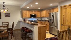 A modern kitchen with wooden cabinets, stainless steel appliances, a bar area, and a chandelier. - Spacious Pet-Friendly 2-Bedroom Condo Tucked in the Woods (Mountain Village)