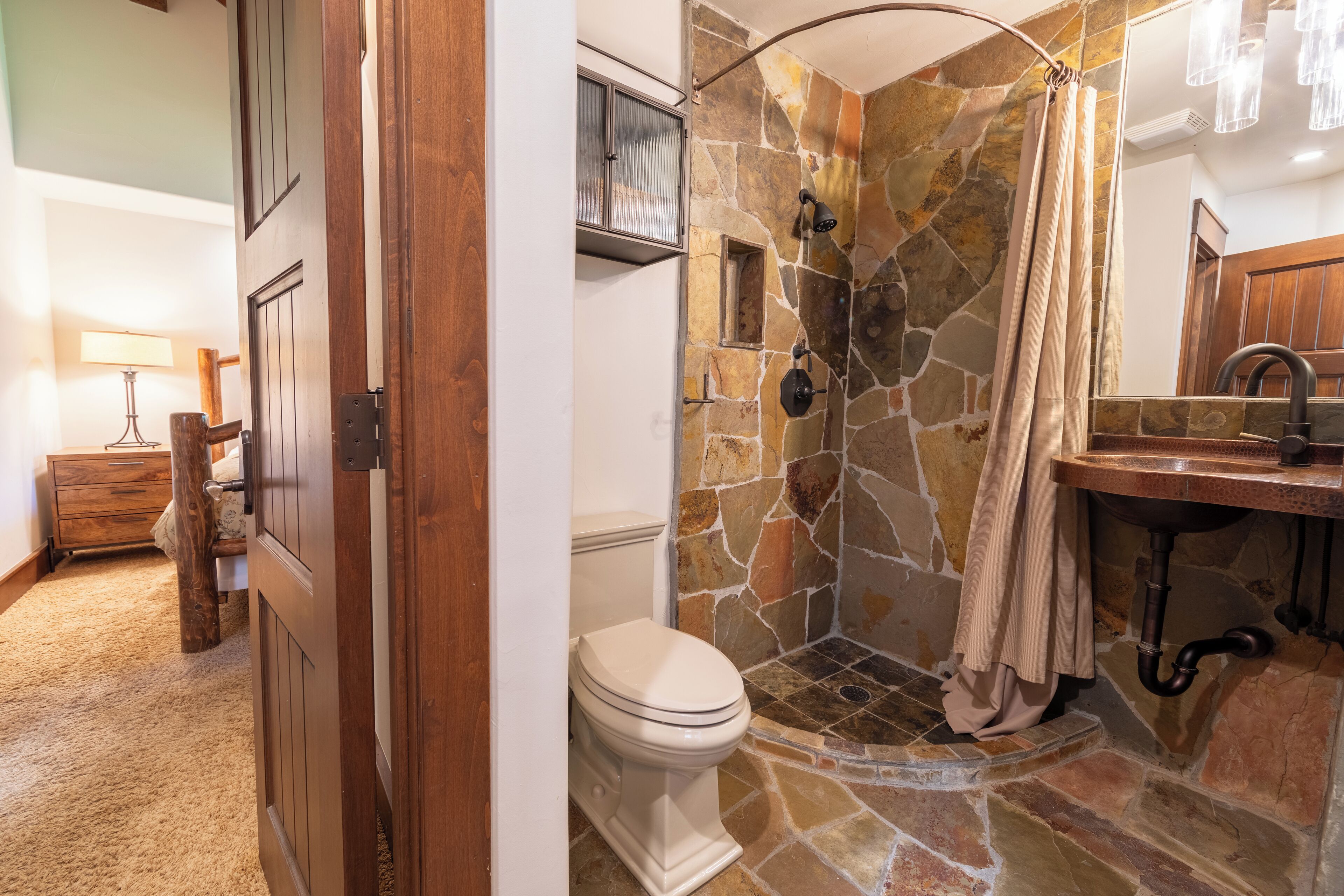 A bathroom with a stone shower, a toilet, and a wooden vanity with a sink.