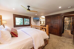 A bedroom with a bed, a ceiling fan, a TV, and a stone wall.