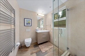 Features a glass shower enclosure, white toilet, and beige vanity with a large mirror.