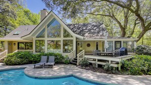 Een huis met een zwembad, een overdekt terras met tuinmeubilair en een groot raam met uitzicht op het zwembad.