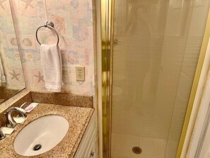Un baño con lavamanos de encimera de granito, un perchero para toallas y una ducha con puerta de cristal.