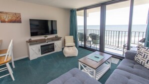 A living room with a TV, seating, a fireplace, and a balcony with a view of the sea. - SEA WORTHY 2 BEDROOM OCEAN FRONT CONDO (GARDEN CITY BEACH)