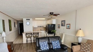 A living room with a black leather sofa, a beige sofa, a wooden coffee table, and a dining area with a kitchen in the background. - COZY LITTLE 1 BEDROOM CONDO (Murrells Inlet)