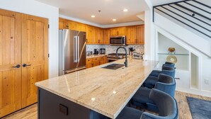 Une cuisine moderne avec des meubles en bois, des appareils en acier inoxydable, un comptoir en granit et un coin bar avec des chaises bleues.