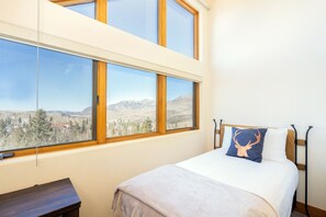 A bedroom with a large window offering a mountain view, a bed with a deer-themed pillow, and a wooden nightstand. - Luxurious Pet-Friendly 4-Bedroom Condo With Stunning Mountain Views & Exquisite (Mountain Village)