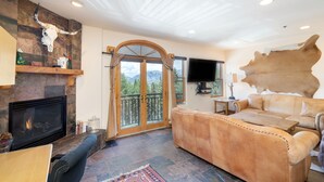 Ein Wohnzimmer mit Kamin, großem Fenster, einer Couch und einem aufgehängten Tierkopf.