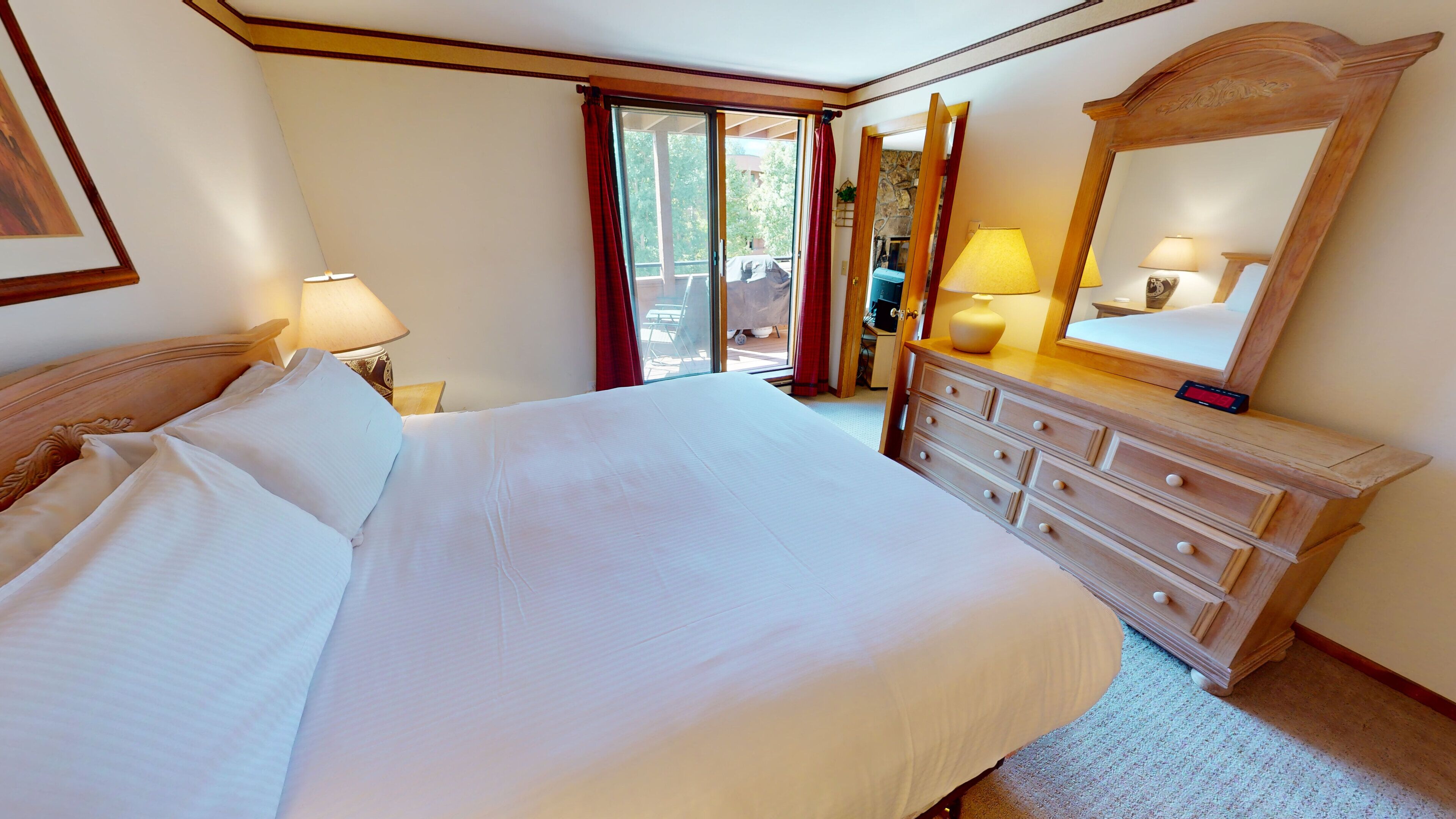 A hotel room with a large bed, a dresser, a mirror, and a sliding glass door to the outside.