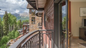 A balcony with a stone wall, a wooden exterior, and a view of mountains and trees.