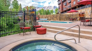 A hot tub with a metal ladder, surrounded by outdoor seating with red cushions, a stone wall, and a view of mountains in the background. - Quiet Lock-Off Room With King Bed in Mountain Village (Mountain Village)