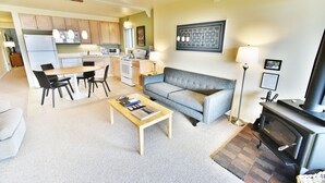 A living room with a sofa, coffee table, and a fireplace. There is a kitchen area with cabinets and appliances. - On Lake, Views! Walk to Amphitheater, Marina, Dining. End Unit, Deck (Dillon)