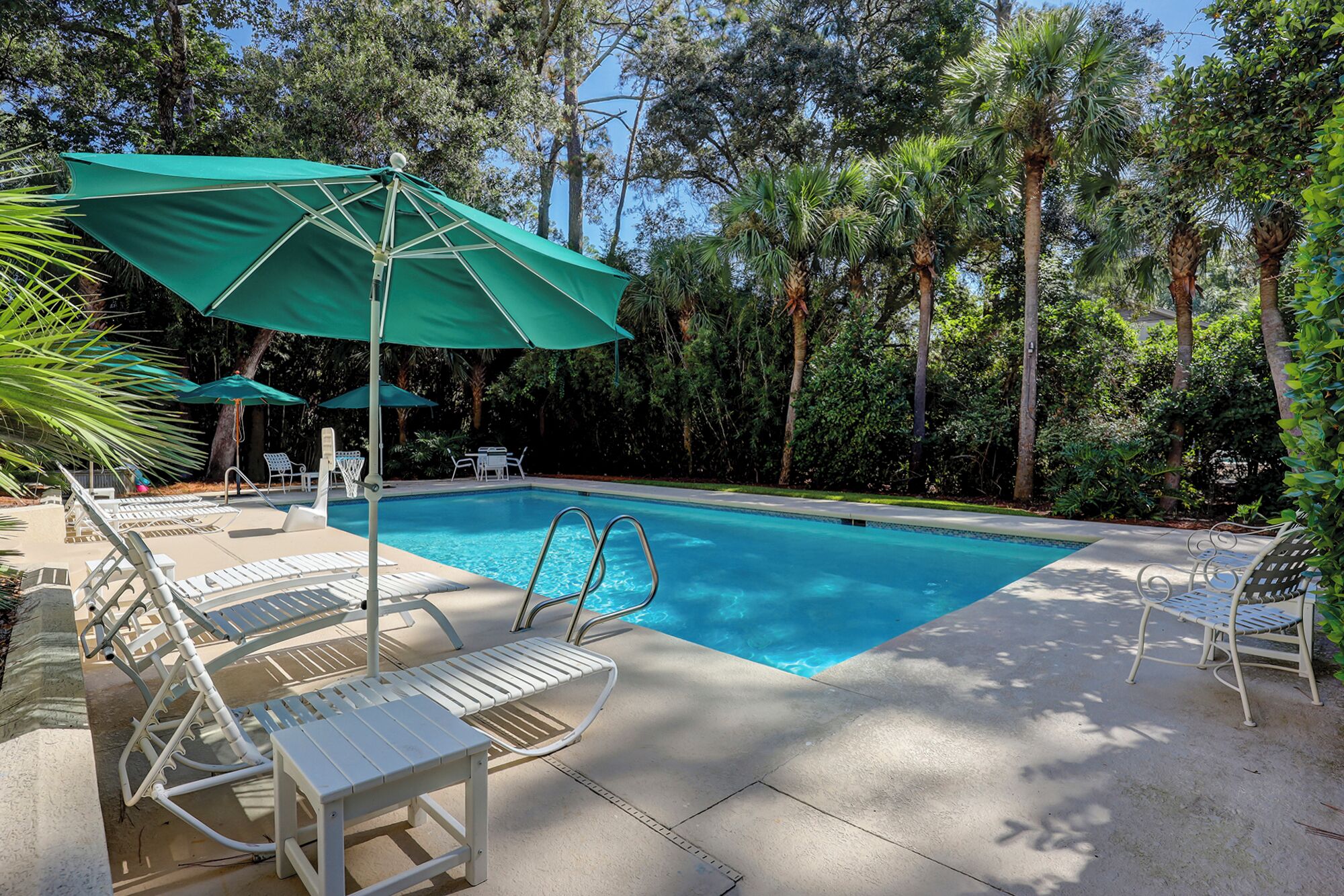 Une piscine entourée d’arbres, avec des chaises longues et des parasols.