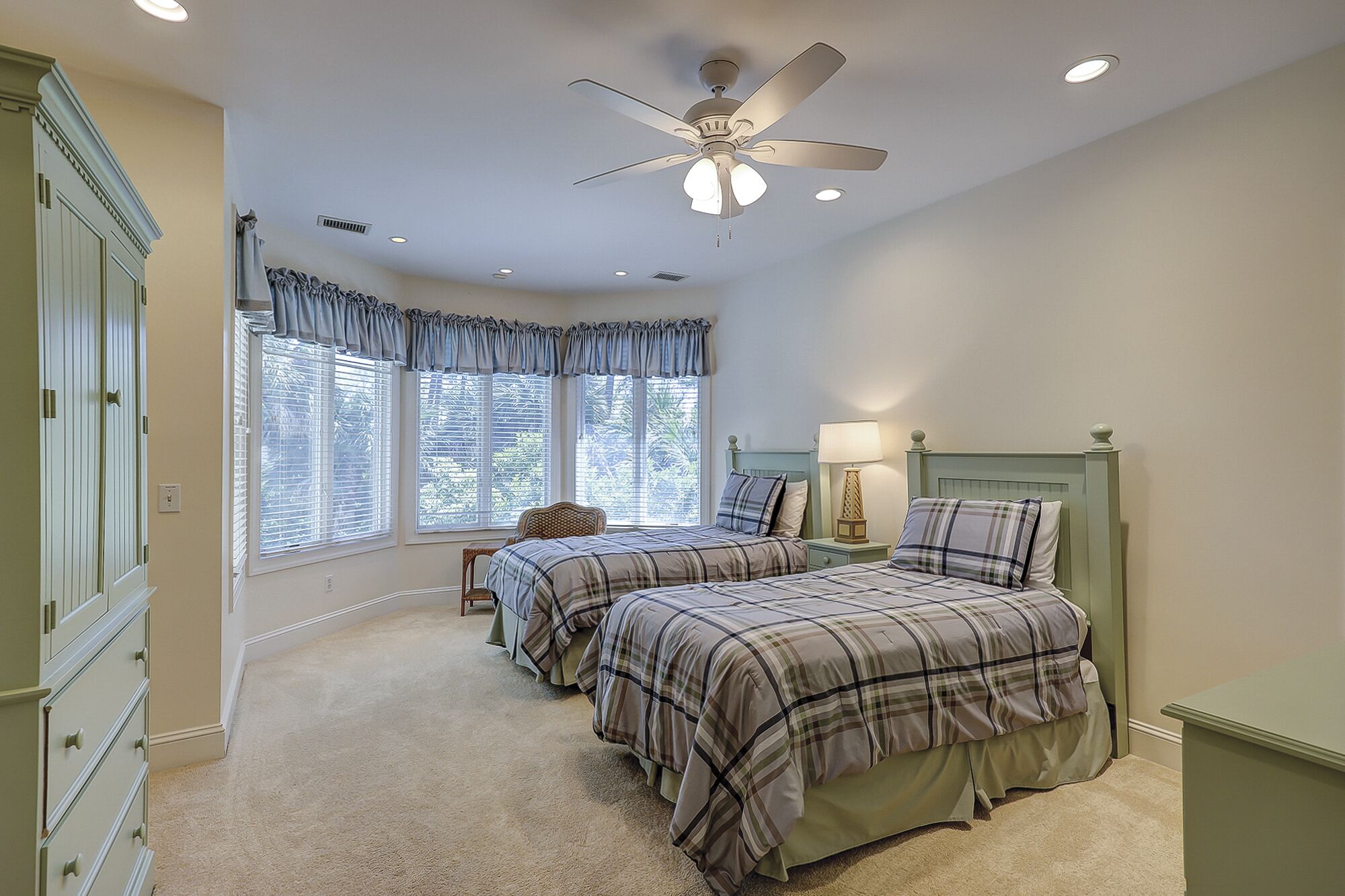 A bedroom with two beds, a ceiling fan, and a window with blinds.