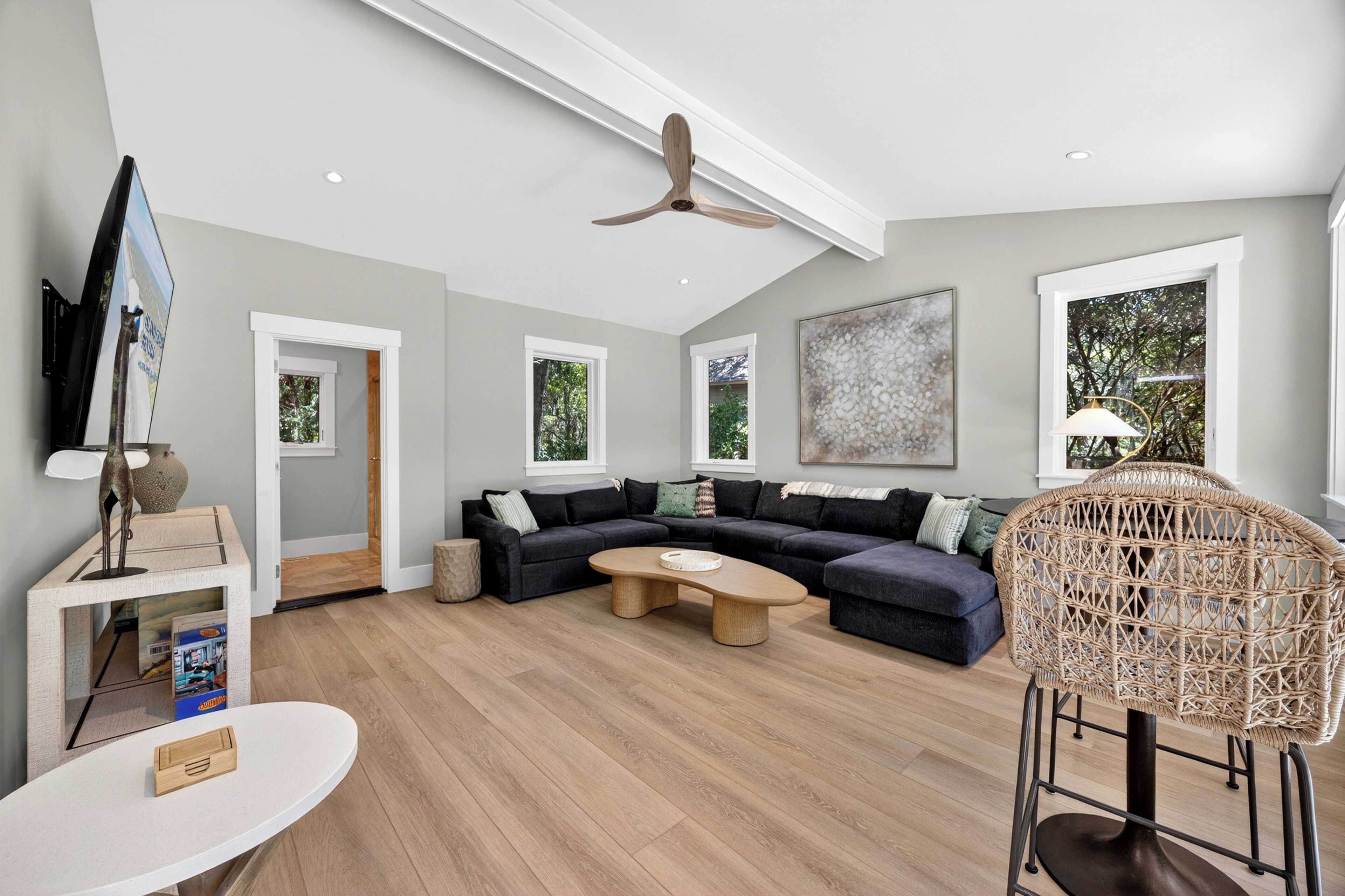 Un salon moderne avec un canapé d’angle, une table basse, un fauteuil en osier et un téléviseur à écran plat.