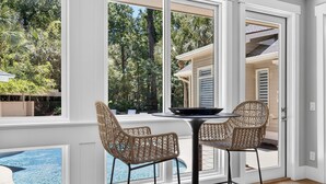 A room with large windows, wicker chairs, a table, and a view of a swimming pool. - Stunning fourth row home in Palmetto Dunes with pool & spa- Beach path nearby (Hilton Head Island)