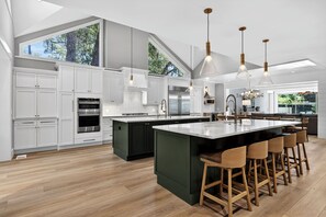 Una cocina moderna con armarios blancos, una isla grande, taburetes de bar e iluminación colgante.