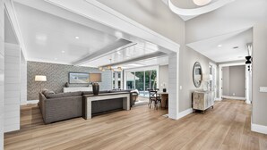A spacious living area with a sofa, a coffee table, and a TV. There is a dining table with chairs and a lamp. The room has wooden flooring and a large window. - Stunning fourth row home in Palmetto Dunes with pool & spa- Beach path nearby (Hilton Head Island)