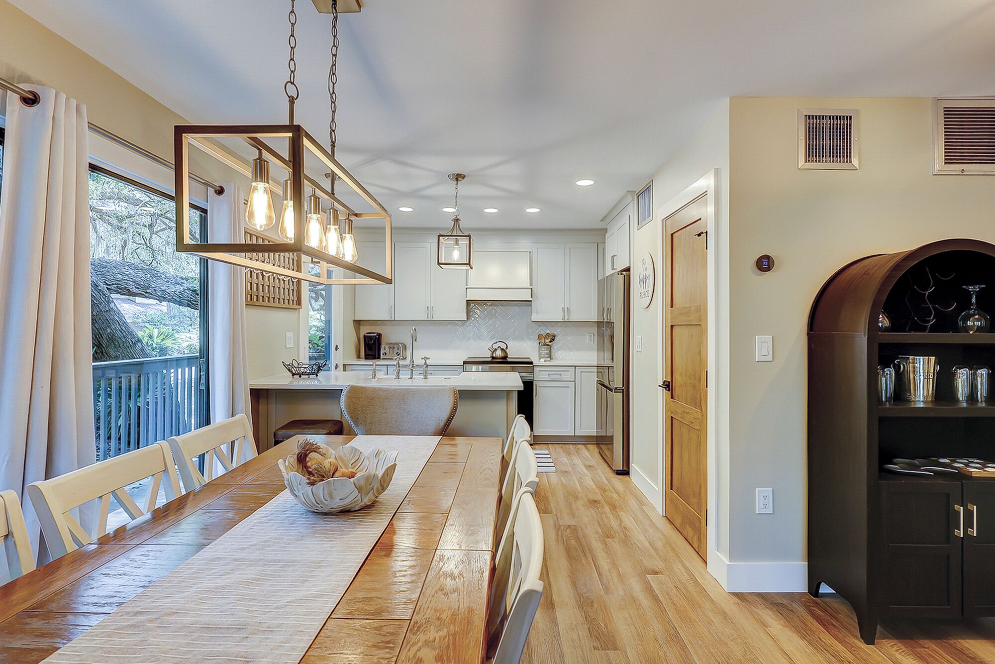 A modern kitchen with a wooden dining table, pendant lights, and a view to the outdoors.