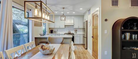 Una cocina moderna con una mesa de comedor de madera, luces colgantes y vistas al exterior.