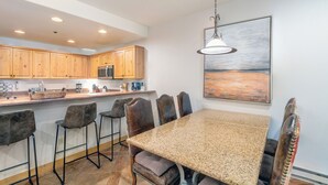 A kitchen with wooden cabinets, a granite countertop, and a dining area with a table and chairs. - Mountainside 2-Bedroom Condo W/Hot Tub, Fireplace, Ski Access (Mountain Village)