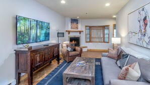 A living room with a fireplace, a large TV, and a sofa. - Mountainside 2-Bedroom Condo W/Hot Tub, Fireplace, Ski Access (Mountain Village)