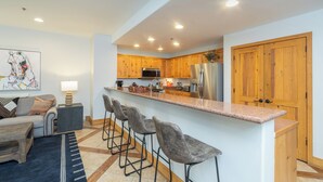 Une cuisine moderne avec des meubles en bois, des appareils électroménagers en acier inoxydable et un coin bar avec des tabourets.