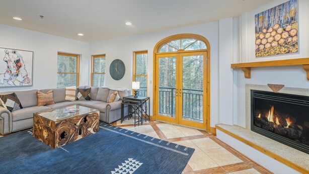 A spacious living room with a fireplace, a sofa set, a coffee table, and a large window with a view of trees. - 3-Bedroom Private Mountainside Condo (Mountain Village)