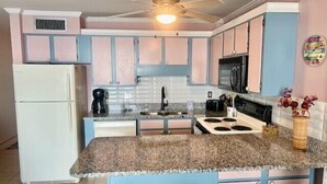 A kitchen with a central island, a refrigerator, a microwave, and a ceiling fan.