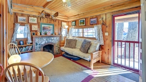 Een gezellig chaletinterieur met een houten plafond, een open haard, een bank en een eettafel.