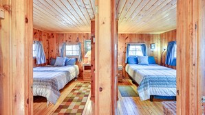 Een houten hut met twee bedden, een geruit vloertje en een raam met gordijnen.