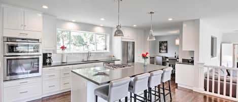 A modern kitchen with white cabinetry, stainless steel appliances, and a large island with bar stools.