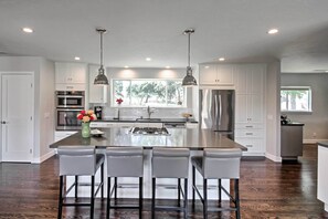Una cocina moderna con una isla central, taburetes de bar, electrodomésticos de acero inoxidable e iluminación colgante.