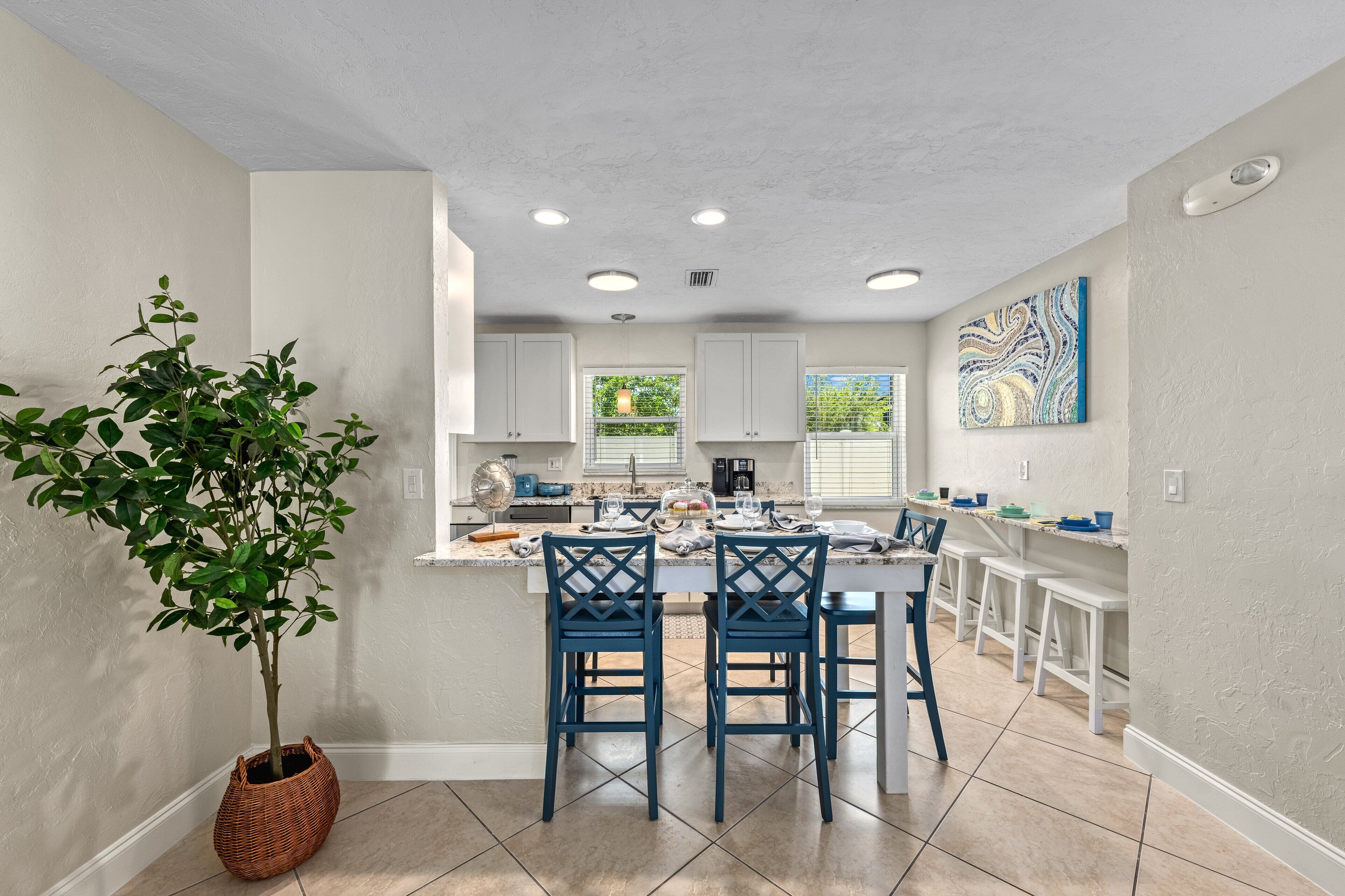 Una cocina moderna con armarios blancos, una isla central con sillas azules y una planta en maceta.