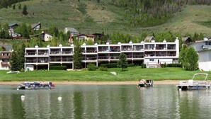 Un hotel de varios pisos con balcones, ubicado junto a un lago con barcos.