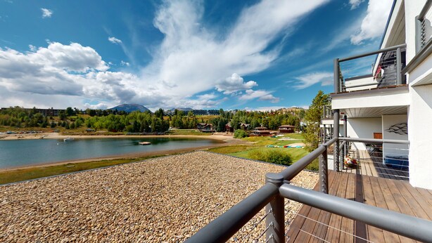 Un balcón con vista a un lago, una terraza de madera y un paisaje montañoso al fondo.