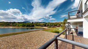 En balkon med udsigt over en sø, en træterrasse og et bjergrigt landskab i baggrunden.